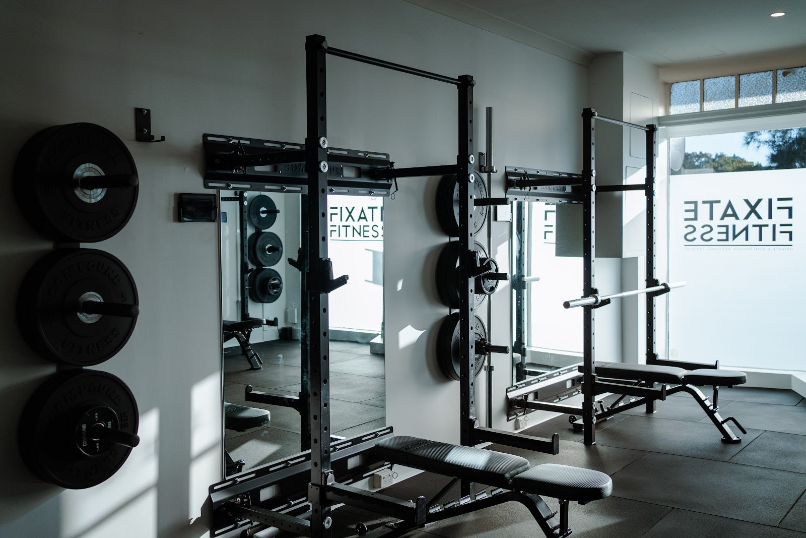 Racks, plate storage and branded window in a boutique gym by Compound Fitness