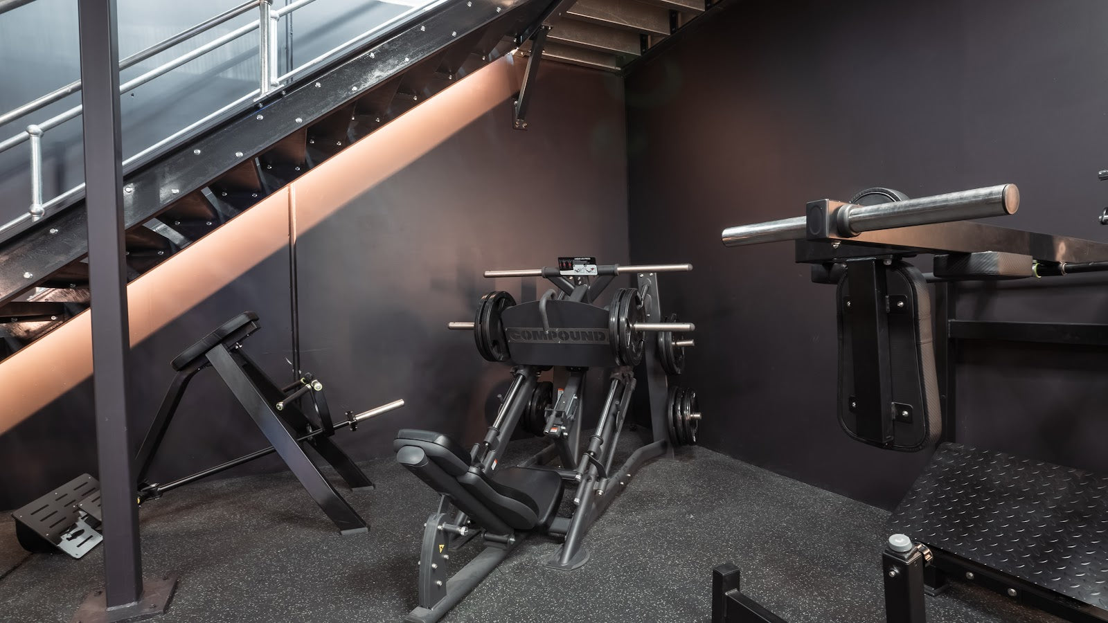 Plate-loaded machines under the stairs in a boutique gym by Compound Fitness