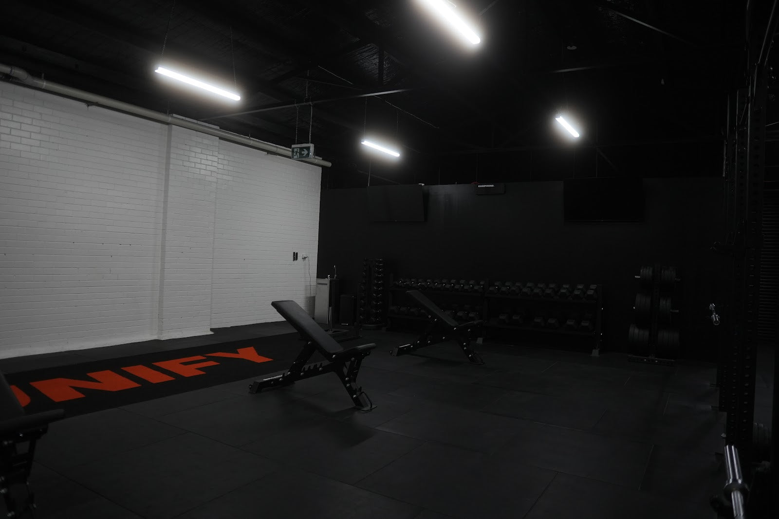 Free weights zone with benches and dumbbell racks in a boutique gym by Compound Fitness