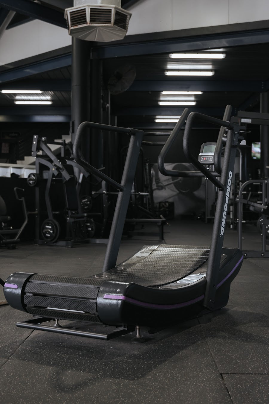 Curved treadmill with plate-loaded floor behind in a 24/7 gym by Compound Fitness