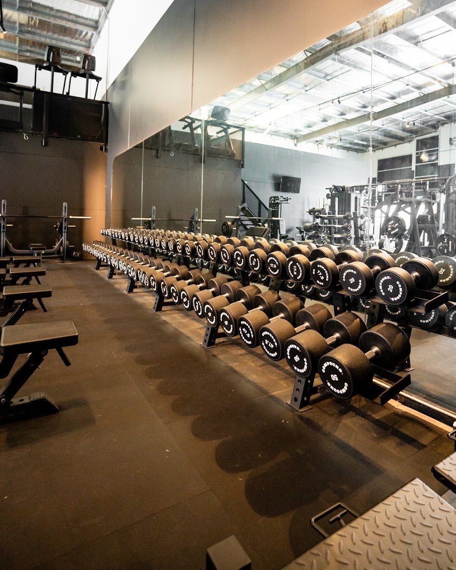 Free weights area with long dumbbell racks in a 24/7 gym by Compound Fitness