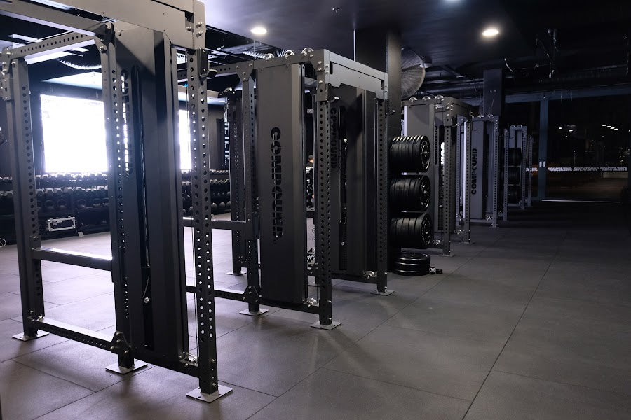 Power rack row across an open 24/7 gym floor by Compound Fitness