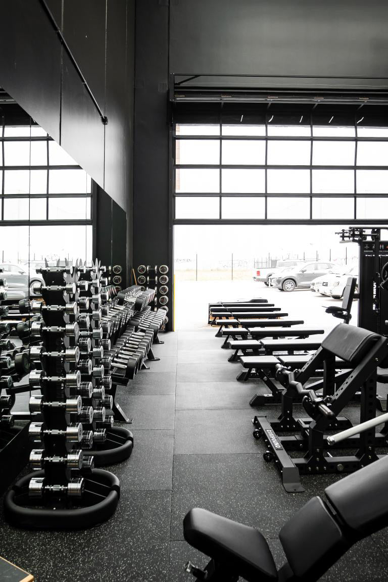 Dumbbell racks and benches by the roller door in a 24/7 gym by Compound Fitness
