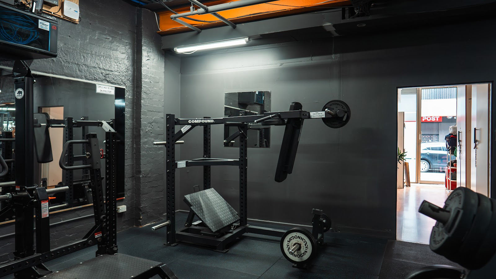 Corner view of a 24/7 gym fitout with rack, plates and mirrors by Compound Fitness