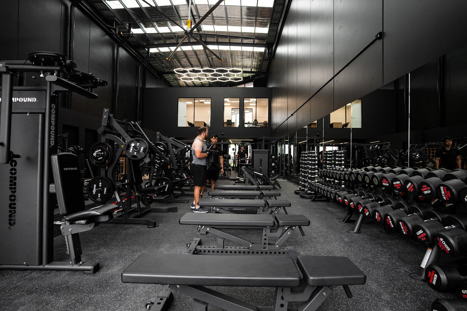 Benches and plate-loaded machines across a 24/7 gym floor by Compound Fitness