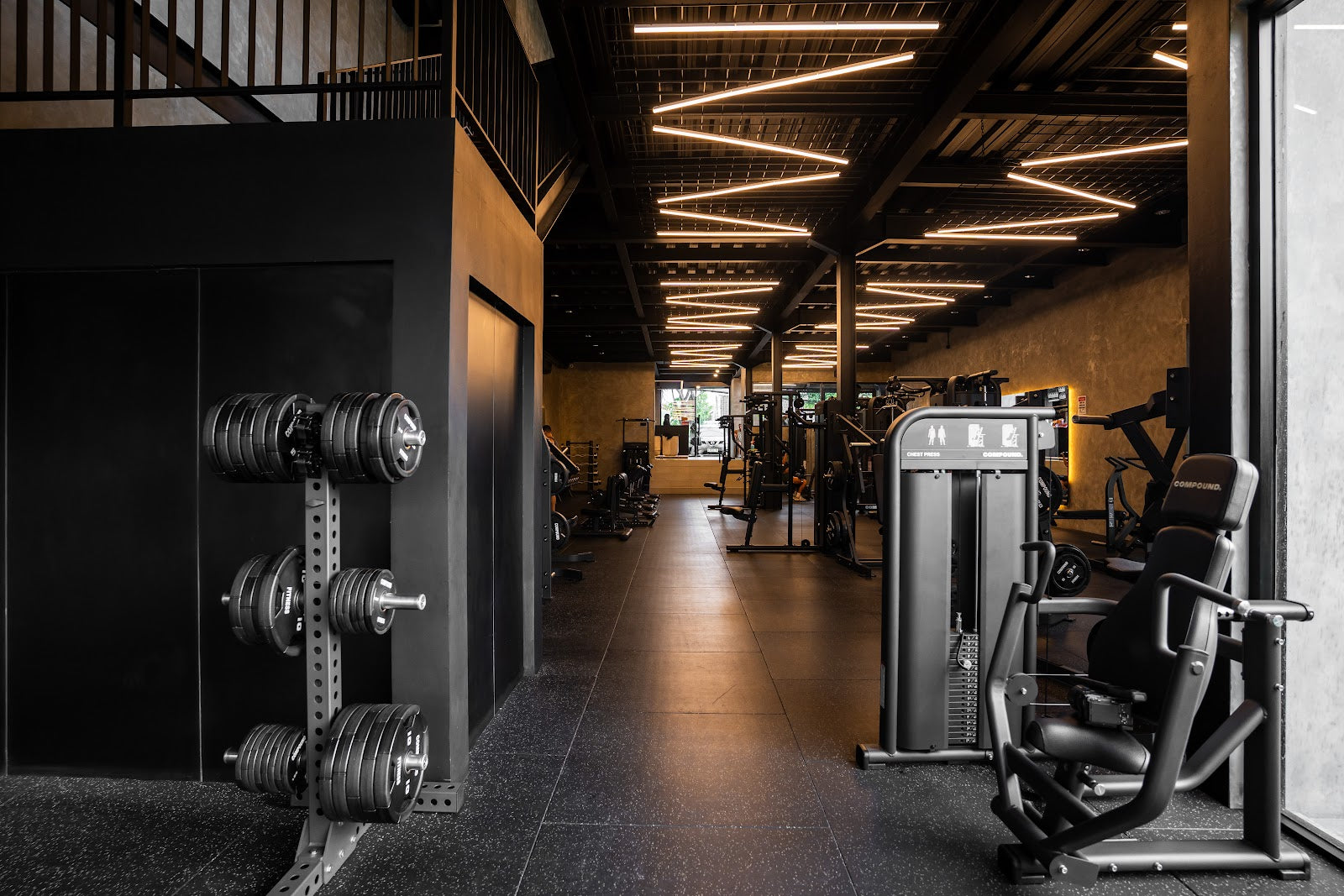 Machine floor and free weights under feature lighting in a 24/7 gym by Compound Fitness
